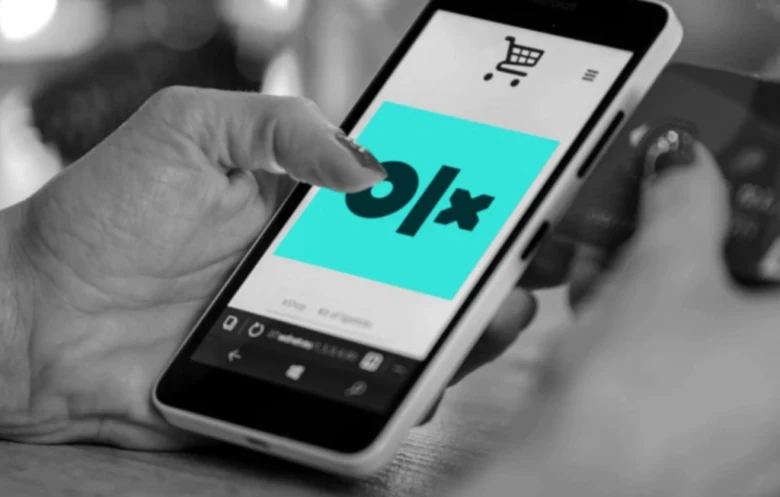 Рука тримає смартфон з додатком OLX для оголошень в Україні.